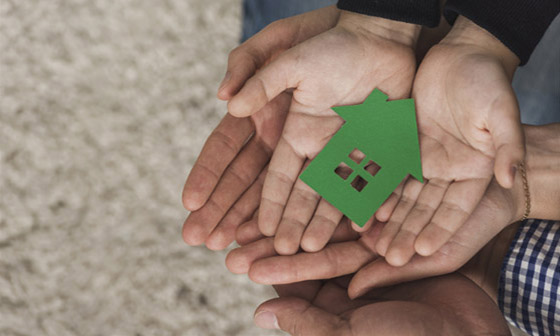 A father and child hold out their hands, they are holding a green model of a house.