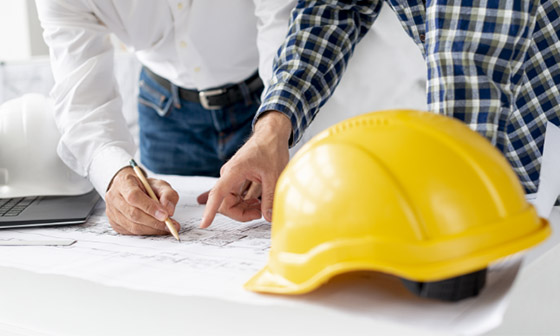 Two workers look over construction plans, their hardhats sit on the table nearby. When you need a reliable contractor, you can depend on Hammer It because your neighbors do, too.