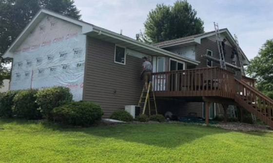 A home with a deck, healthy lanw and shrubs. Contractors work on the house on ladders