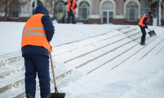 Workers in orange vests clear snow off stairs
