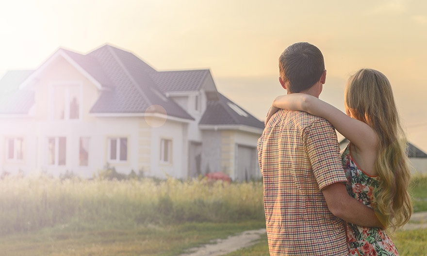 A father holds his daughter. They are looking at their new home, a white house with a gray roof and modern windows.