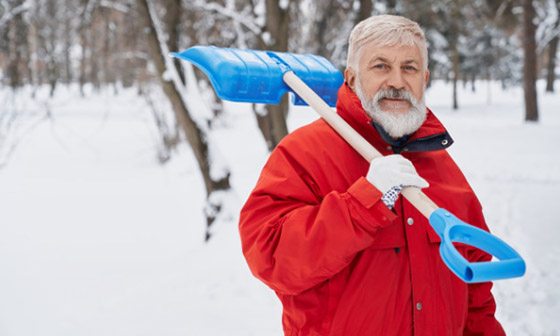 A man in a read jacket holds a snow shovel